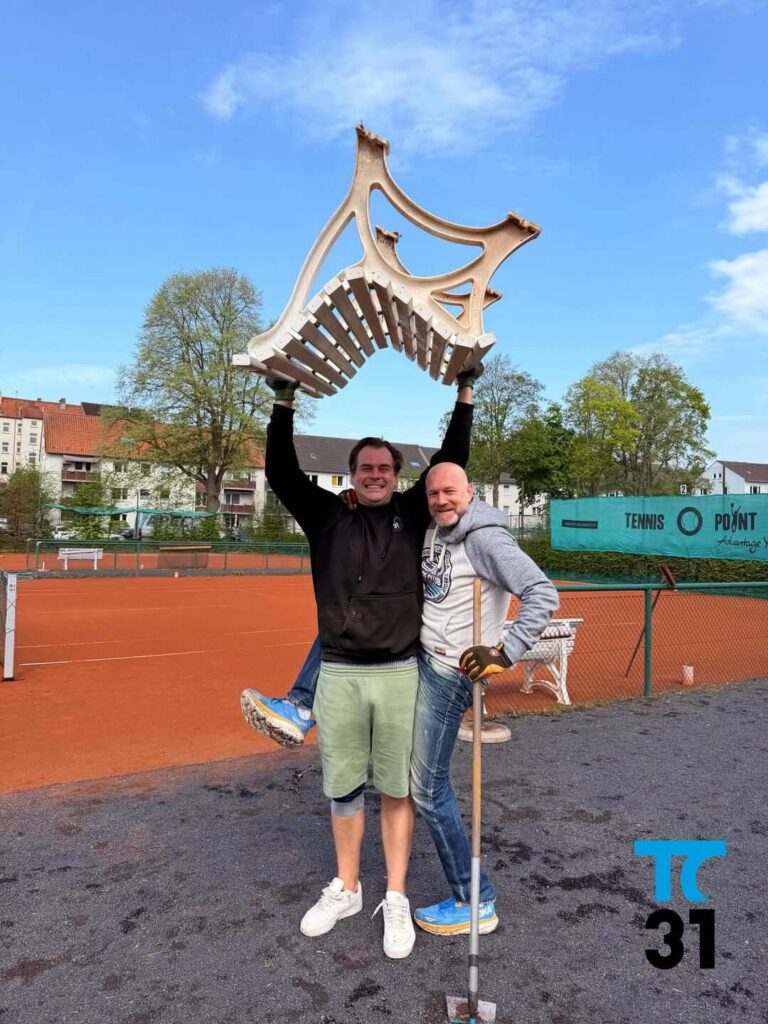 Ein Helfer des TC31 Kassel hebt eine schwere Holzbank an, um sie an ihren Platz zu stellen oder darunter zu fegen.