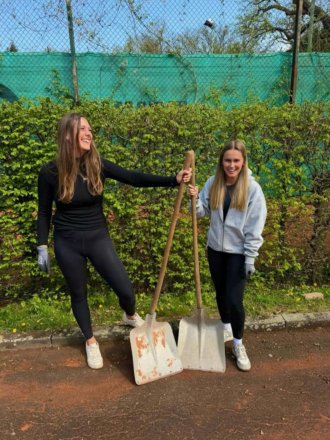 Zwei lachende Helferinnen des TC31 Kassel mit großen Schaufeln beim Arbeitseinsatz auf dem Tennisplatz.