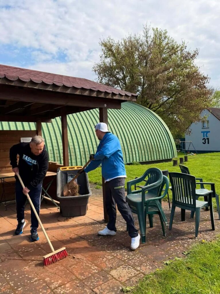 Vereinsmitglieder reinigen die gepflasterten Flächen vor dem Unterstand auf der Tennisanlage.