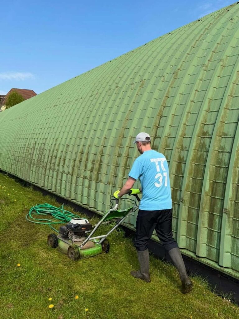 Ein Helfer im Vereins-Shirt des TC 31 mäht den Rasen neben der Halle.