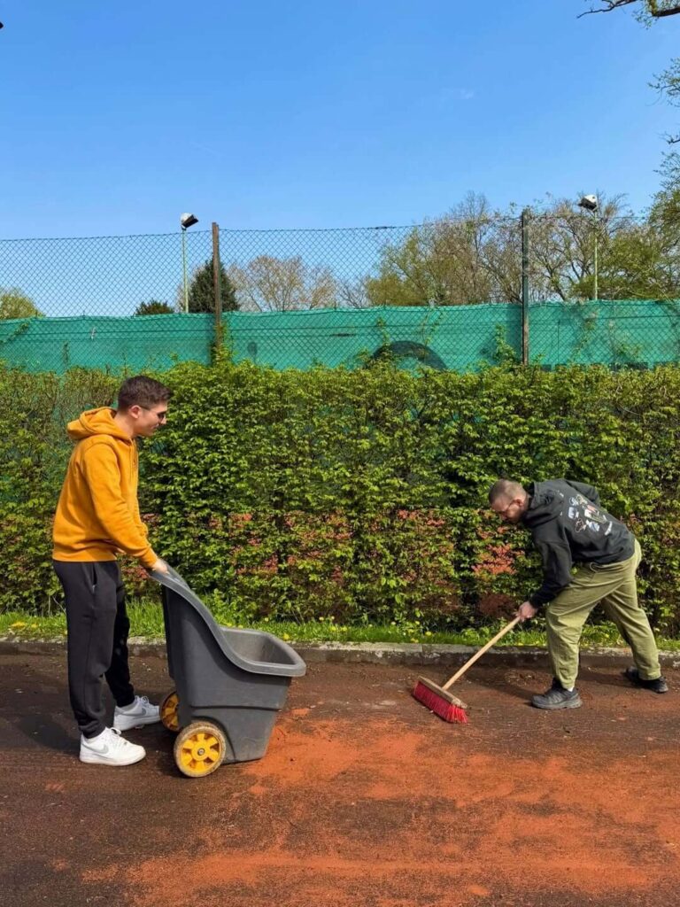 Zwei Helfer bereiten den Sandplatz beim TC31 Kassel vor, indem sie die rote Asche fegen.